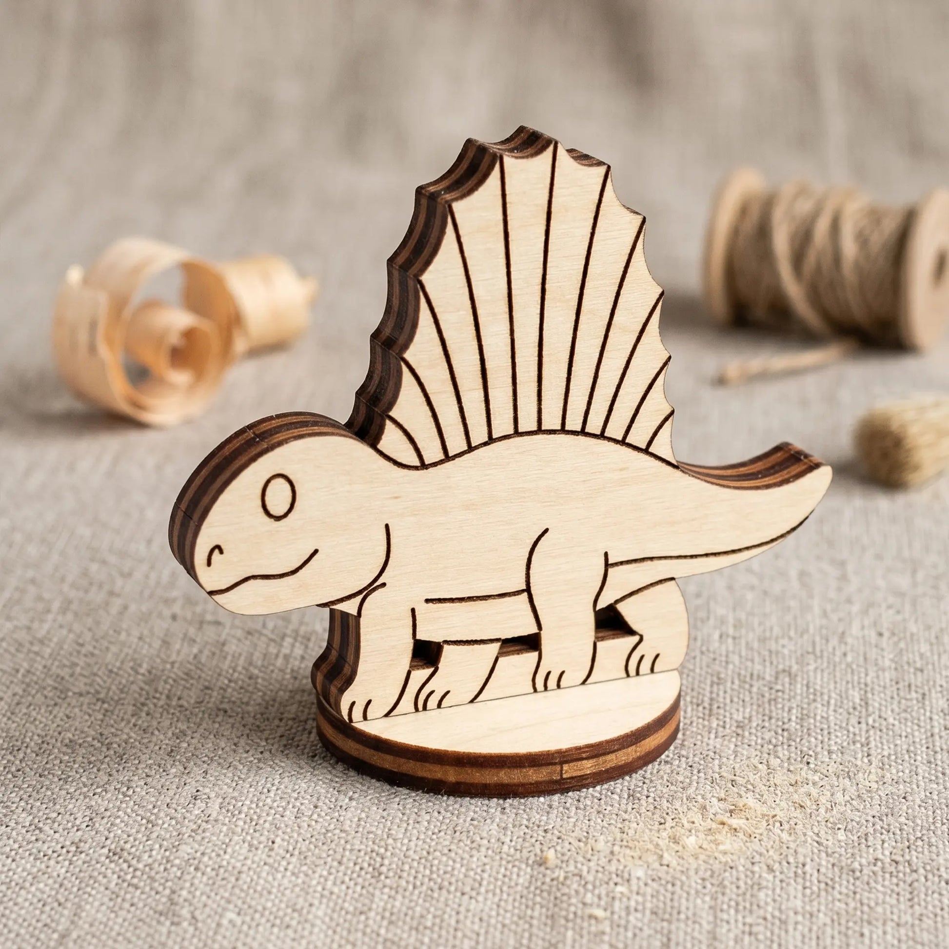 A single laser cut plywood dimetrodon dinosaur figurine on a round stand with wood shavings blurred in the background.