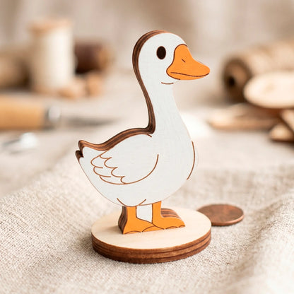 Painted laser cut plywood goose toy with a white body and orange beak standing on a linen cloth.