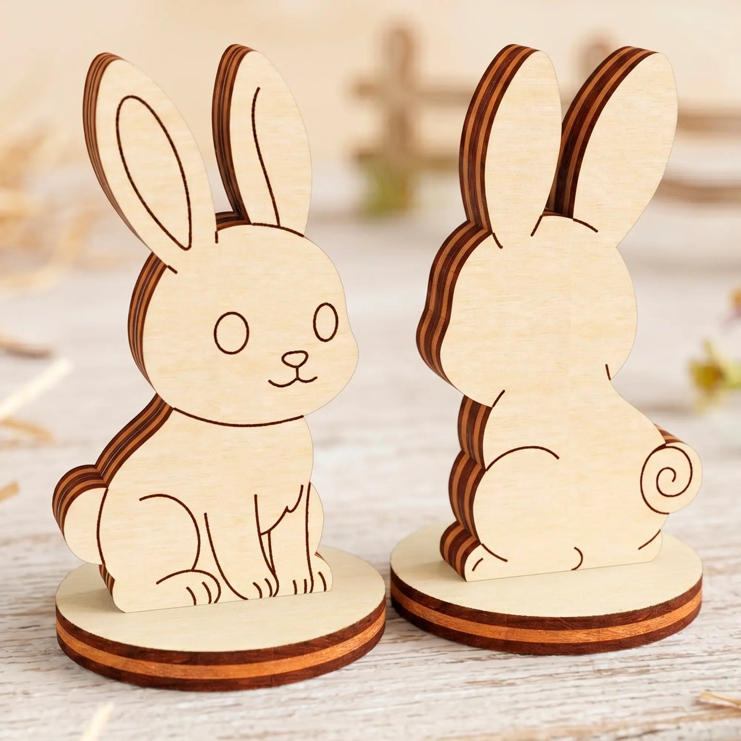 Two laser cut plywood rabbit figurines on round stands shown from the front and back, standing on a light wooden table.