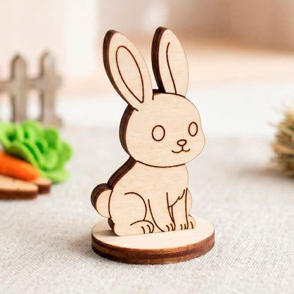 A laser cut plywood bunny figurine on a round base with a blurred miniature fence and felt carrot in the background.