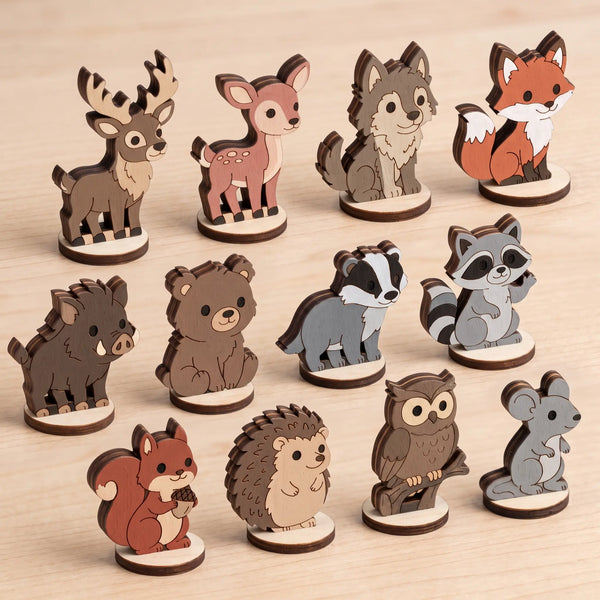 High angle view of 12 hand-painted laser cut plywood forest animal figurines on round wooden stands on light desk
