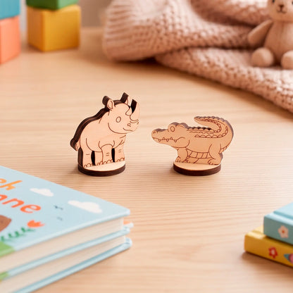 Close-up of two small laser-cut plywood animal figurines, a rhino and a crocodile, standing on a wooden surface.