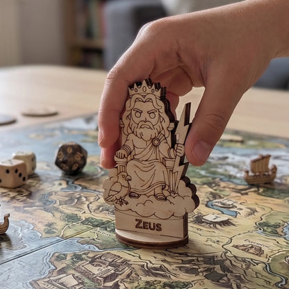 Scale view of a hand placing the laser cut plywood Zeus figurine on a tabletop RPG board game map of ancient Greece