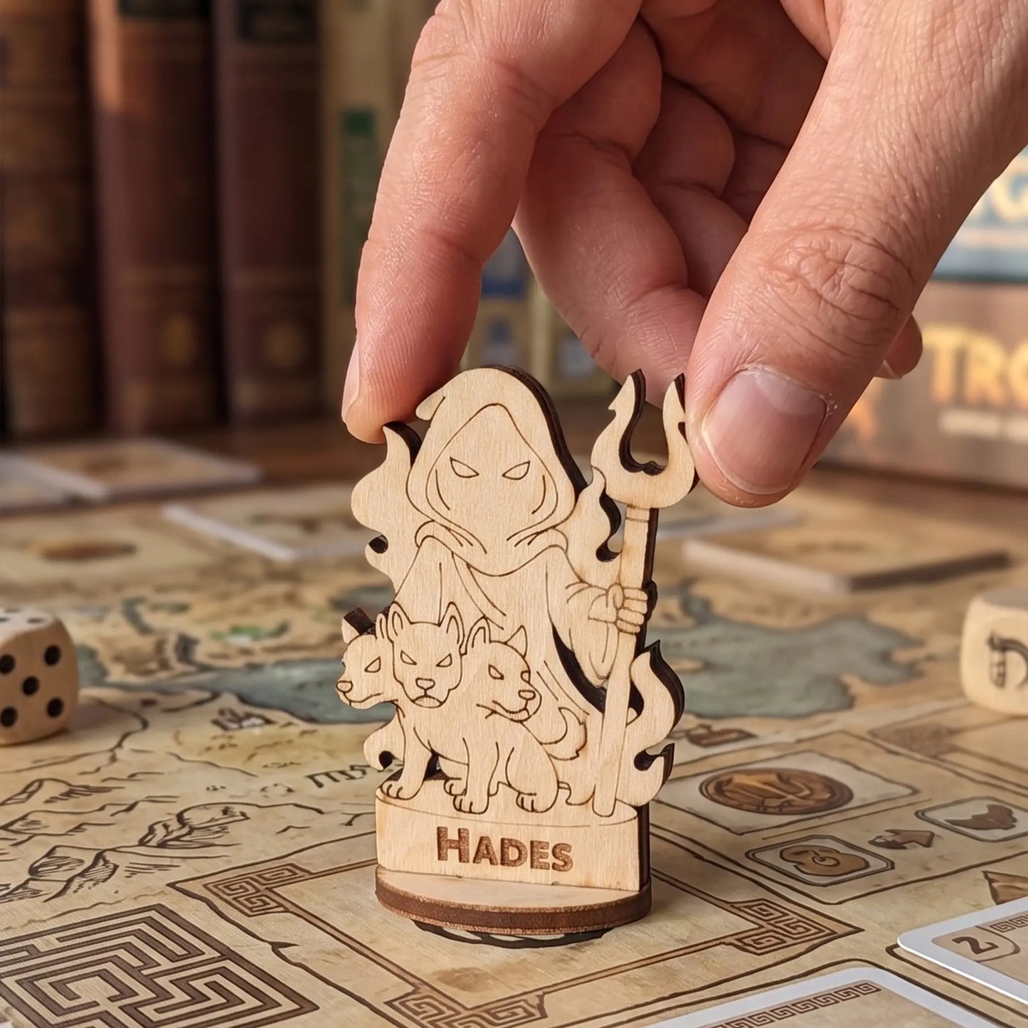 Adult hand placing a laser cut plywood Hades figurine on a detailed board game map with Greek patterns and RPG tokens