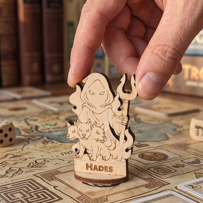 Adult hand placing a laser cut plywood Hades figurine on a detailed board game map with Greek patterns and RPG tokens