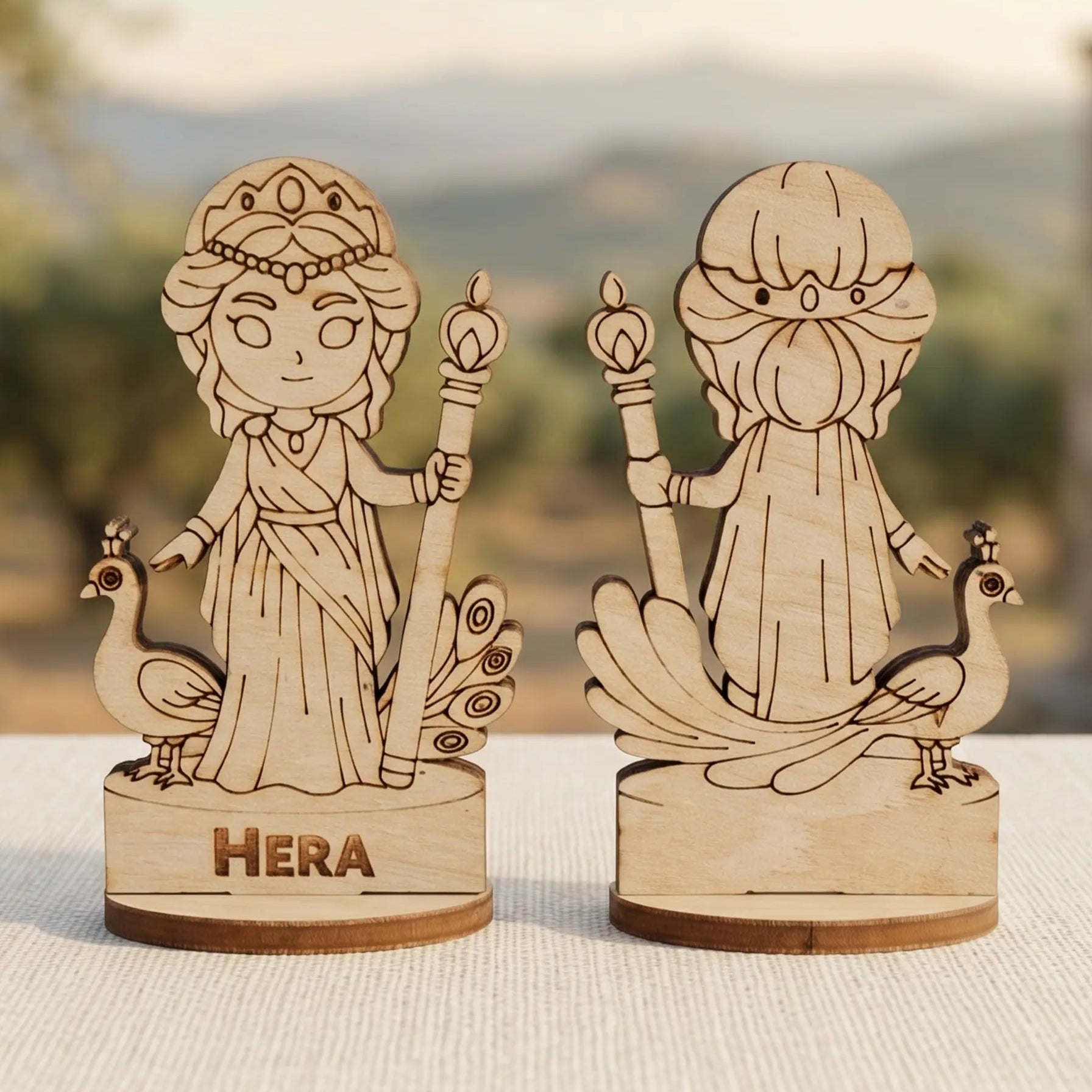 Laser cut plywood Hera miniature front and back views with peacocks and staff, standing against blurred ancient Greek ruins.