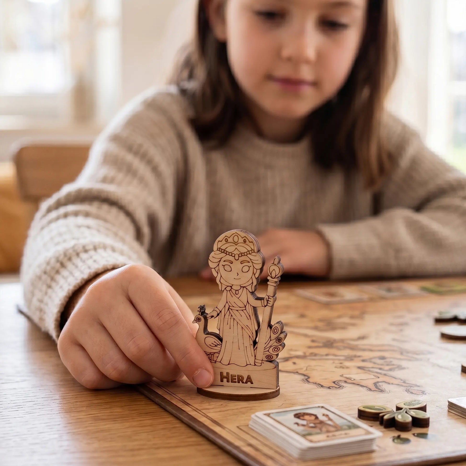 A young child playing with a detailed laser cut plywood Hera miniature on a colorful tabletop RPG board game map with dice
