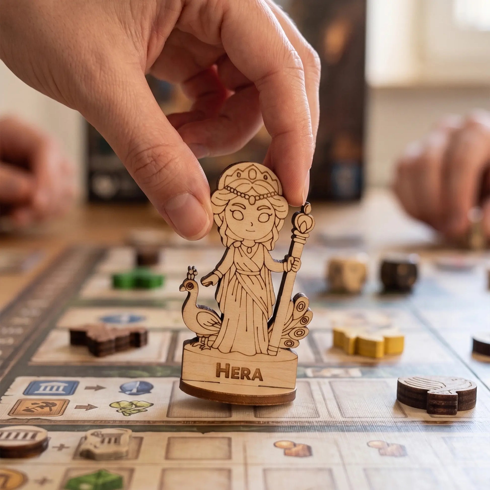 An adult hand carefully moving a laser cut plywood Hera figurine across a grid-based tabletop board game during a session.