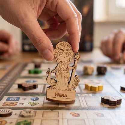 An adult hand carefully moving a laser cut plywood Hera figurine across a grid-based tabletop board game during a session.