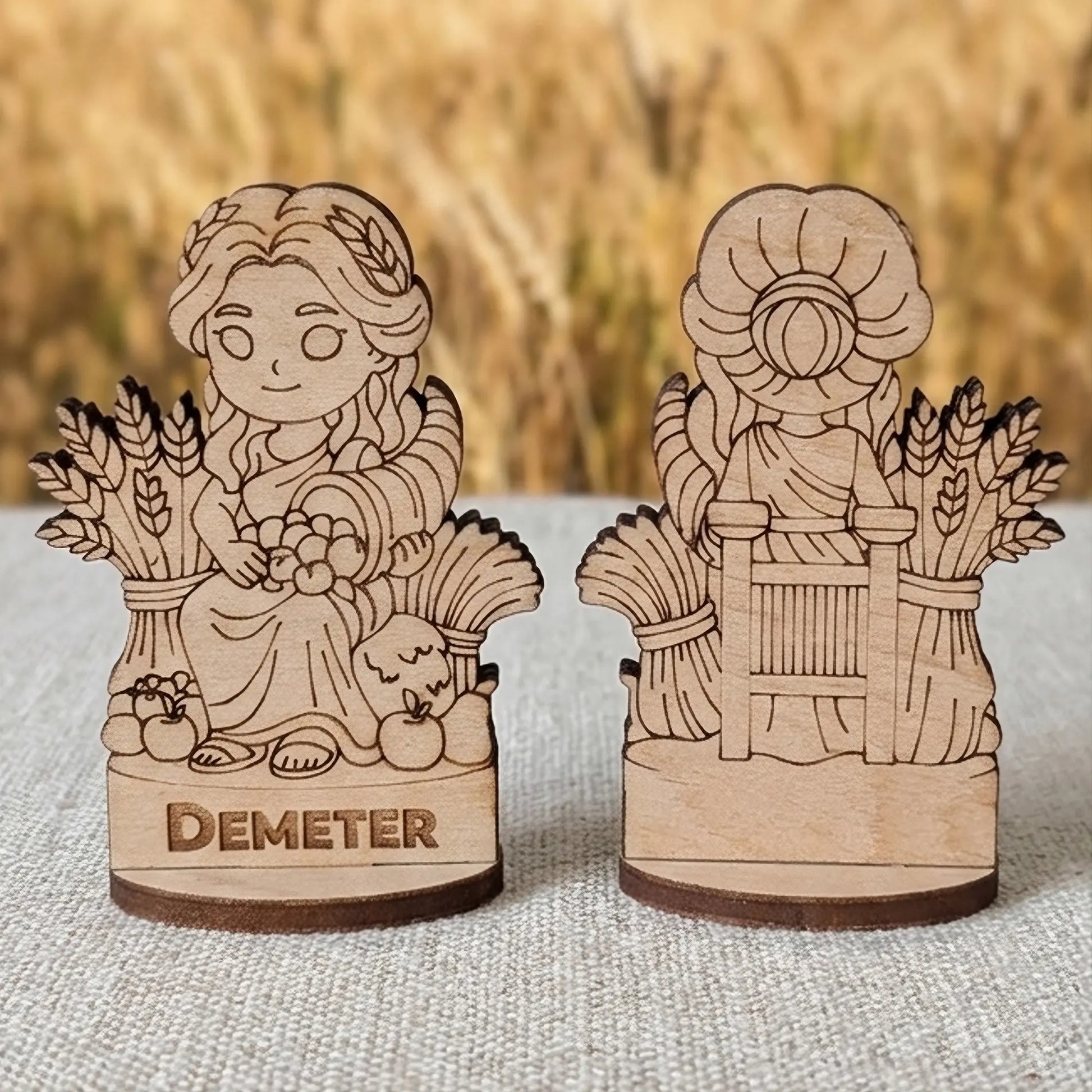Front and back views of a laser cut plywood Demeter miniature with wheat and fruit against a blurry summer field background.