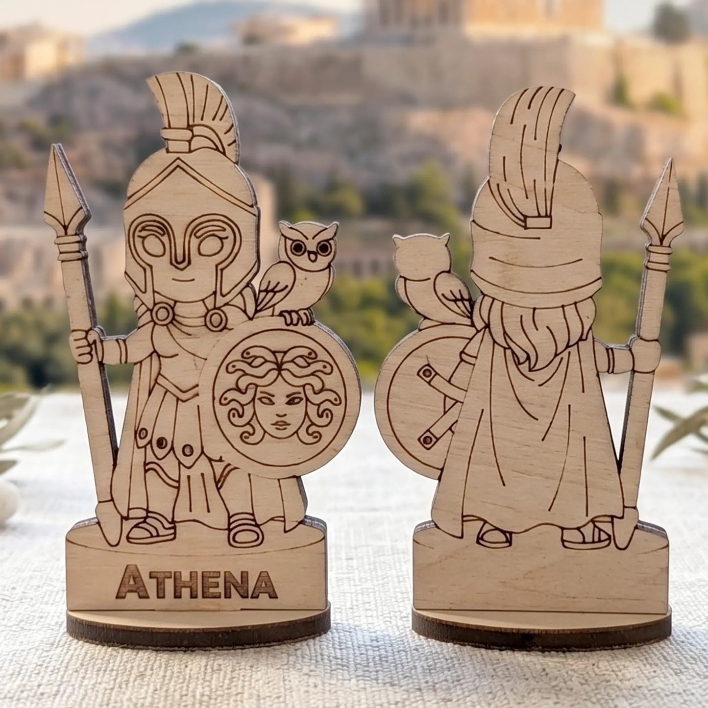 Front and back views of a laser cut plywood Athena figurine with spear, owl, and Medusa shield against blurred ancient ruins.