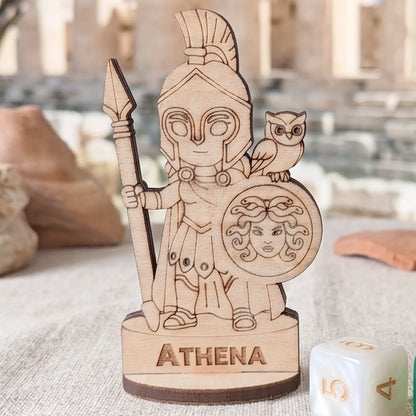 Front view of laser cut plywood Athena miniature standing next to a white gaming die to show its small handcrafted scale.