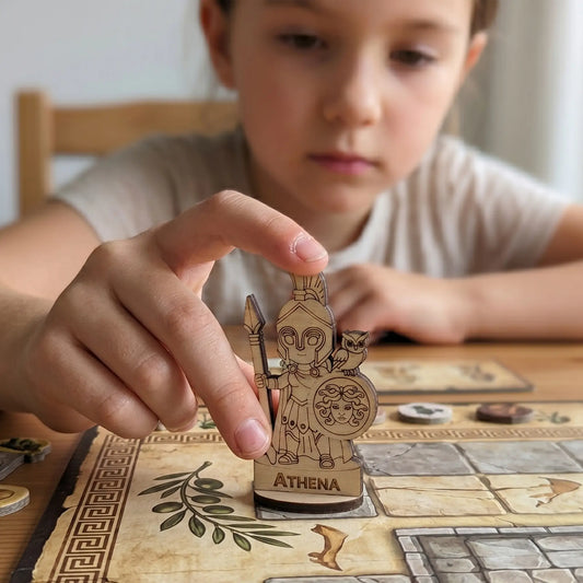 A child's hand moves the laser cut plywood Athena figurine across a colorful board game map during an educational session