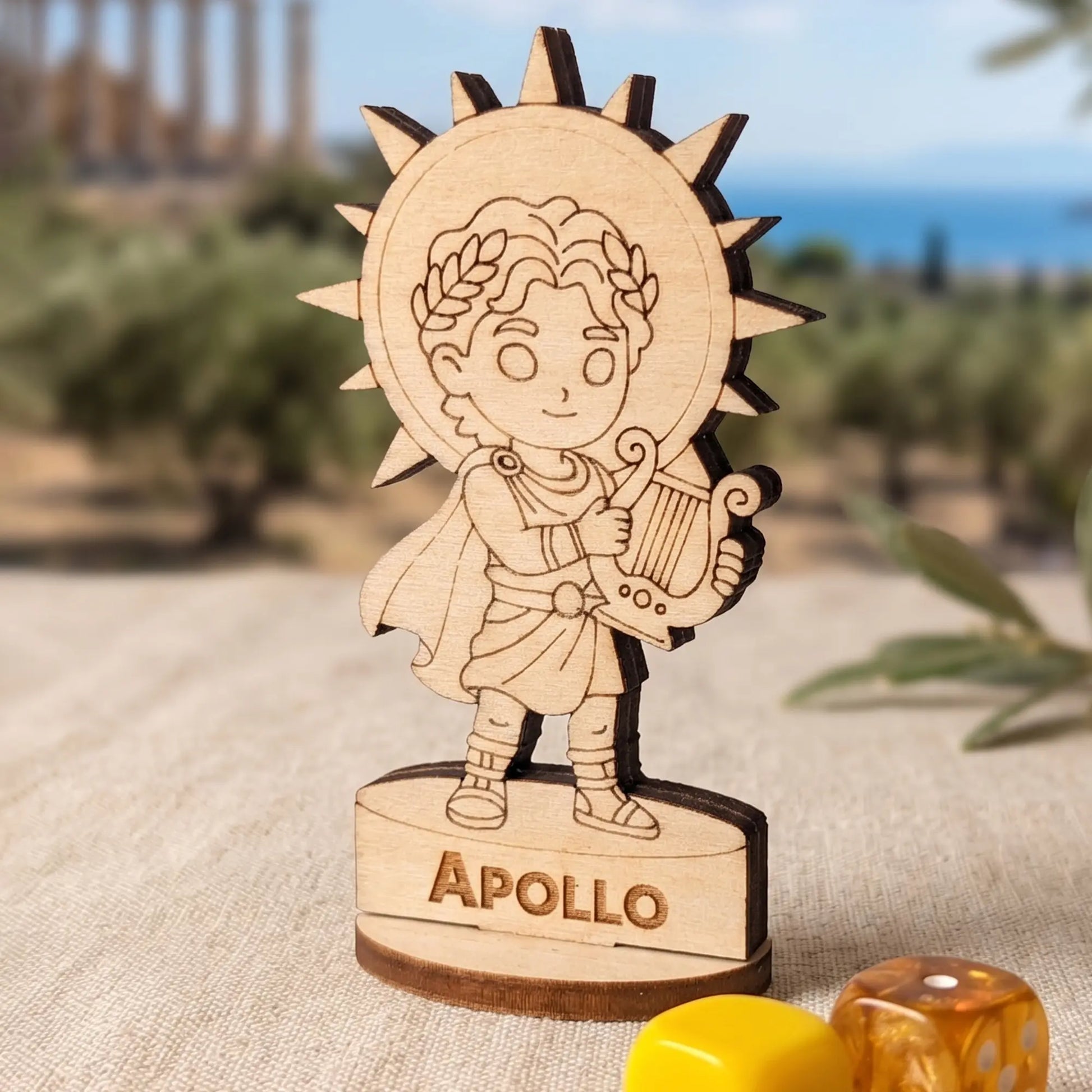 Laser cut plywood Apollo miniature on a wooden table with blue and white RPG dice for tabletop gaming scale reference.