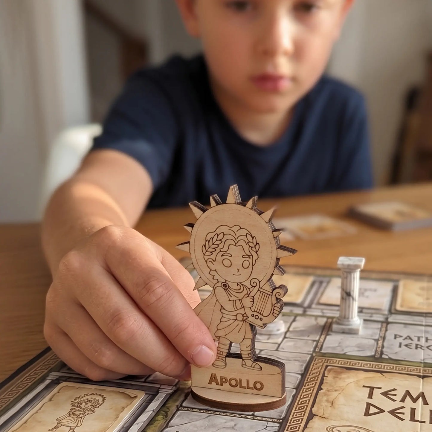 A child's hand moving a laser cut plywood Apollo figurine across a colorful board game map during a tabletop RPG session.