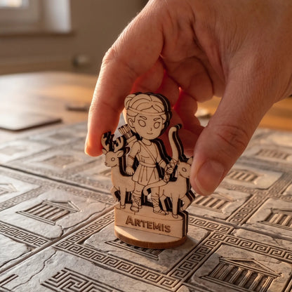 Adult hand placing a laser cut plywood Artemis figurine on a grid-based board game tile with engraved Greek temple motifs