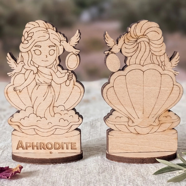 Front and back views of a laser cut plywood Aphrodite miniature in a shell with doves and mirror against blurred ruins