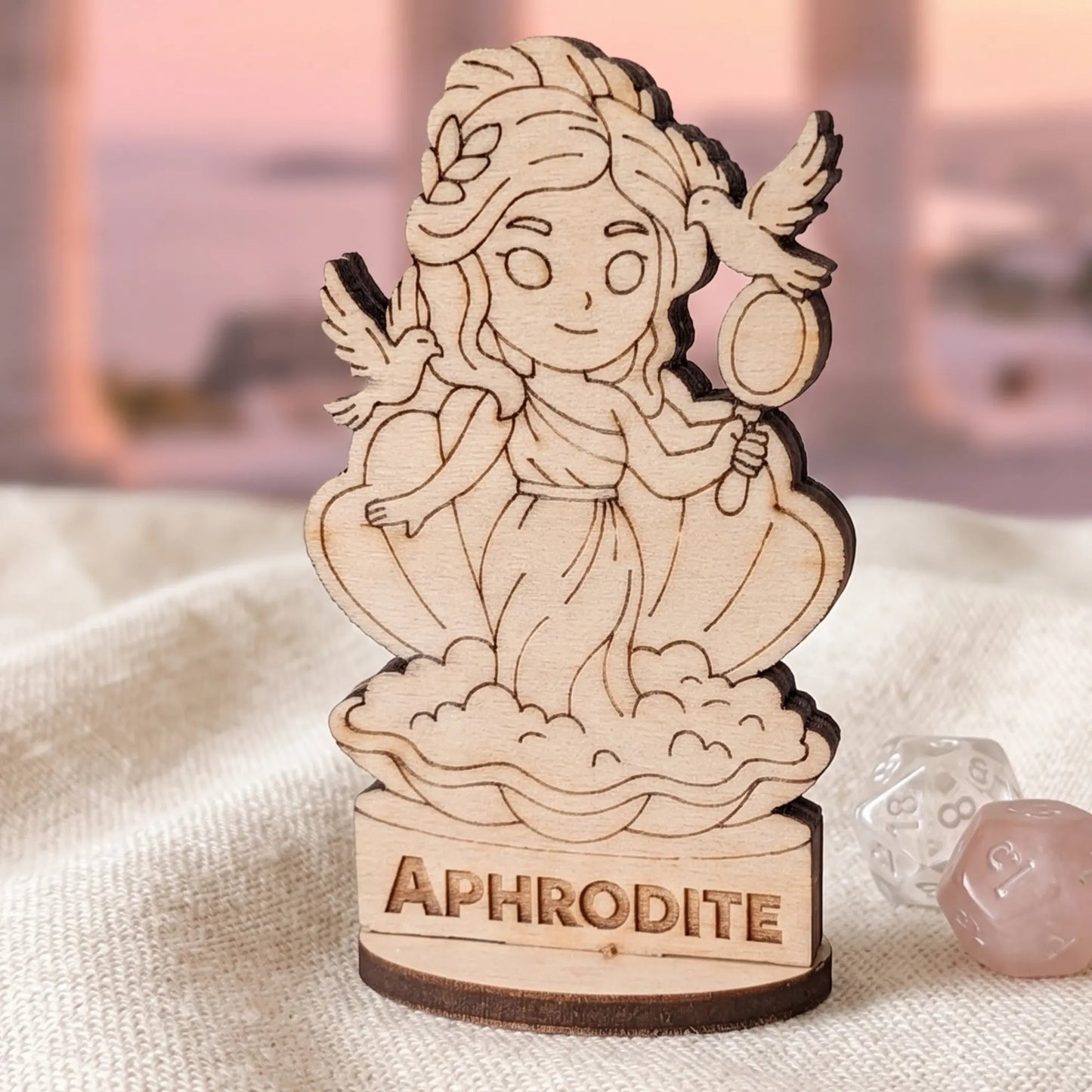 Macro shot of laser cut plywood Aphrodite miniature on fabric with clear RPG dice for tabletop gaming scale reference
