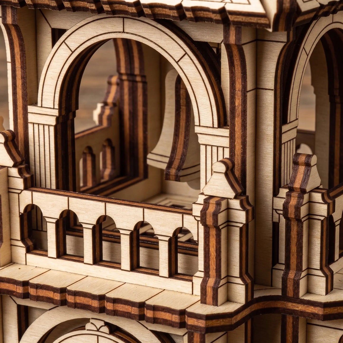 Close-up of the delicate upper balcony arches and a tiny hanging bell inside a layered laser cut plywood tower toy.
