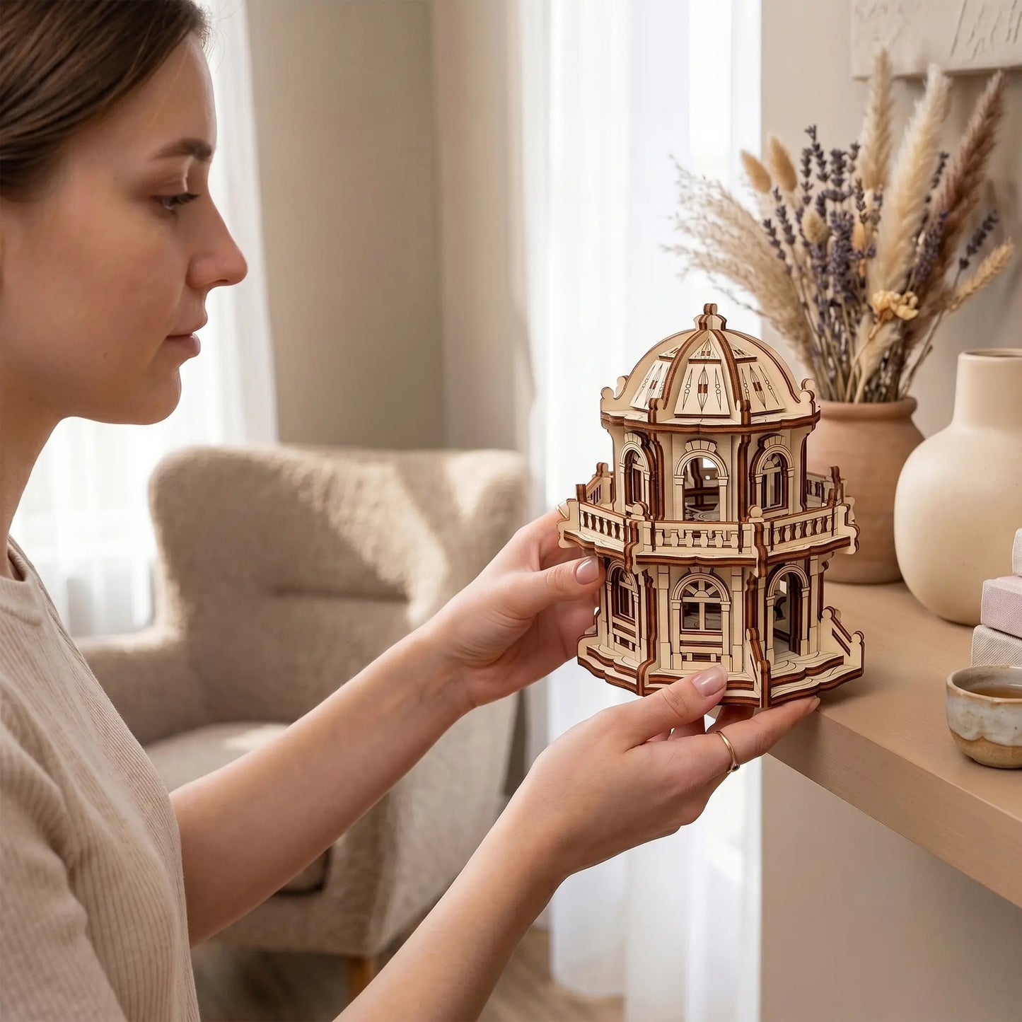 A woman holding a miniature dome palace of laser cut plywood, showcasing its intricate handheld scale and design.