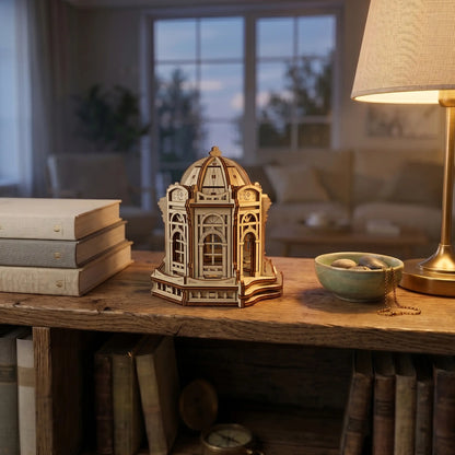 Miniature wooden rotunda house of laser cut plywood on a floating shelf near a dry flower vase and ink quill.