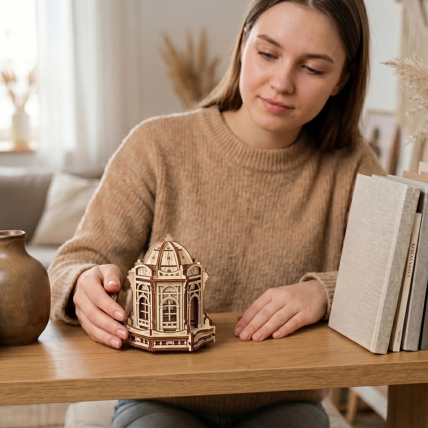 A woman sitting at a table with books, admiring a miniature moon fairy dome palace made of laser cut plywood.