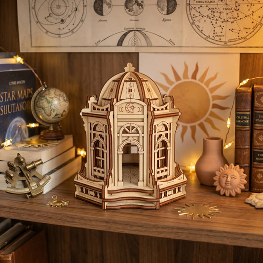 Miniature laser cut plywood moon palace on a desk surrounded by a globe, star maps, and celestial home decor.