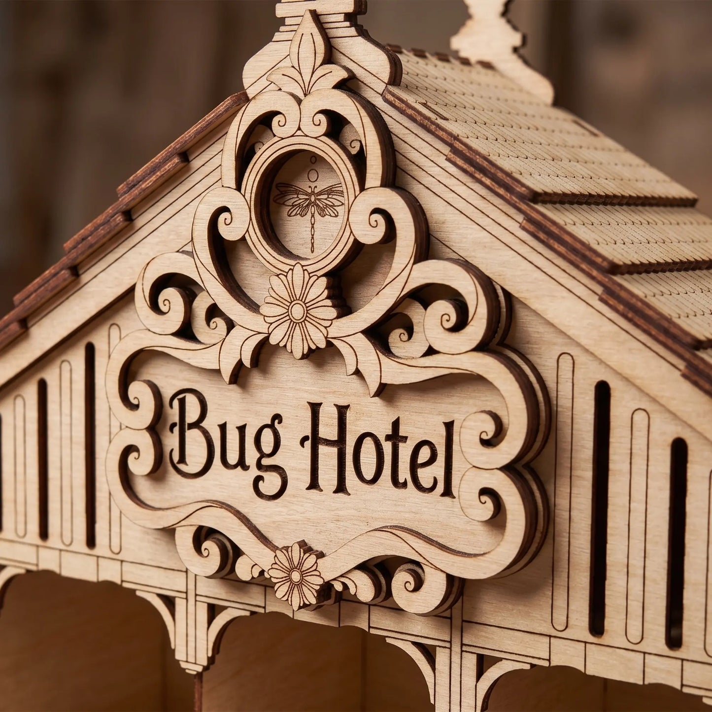 Close-up of the engraved sign and dragonfly emblem on a laser cut plywood bug hotel house roof with dark edges.