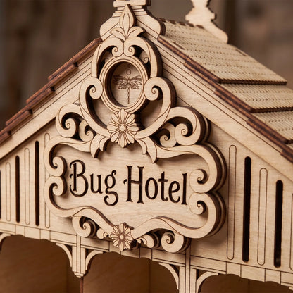 Close-up of the engraved sign and dragonfly emblem on a laser cut plywood bug hotel house roof with dark edges.