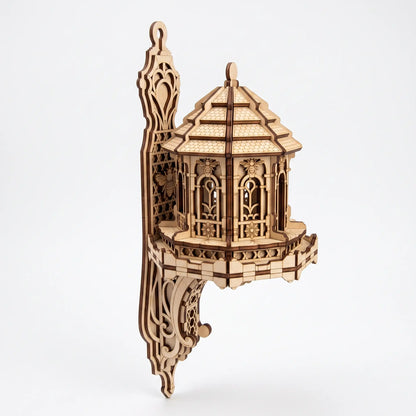A laser-cut wooden wall-mounted pavilion house with intricate openwork details, shown against a plain light gray background.