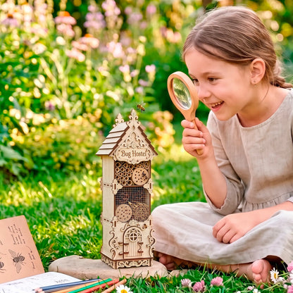 A child sitting on the grass in a garden, examining a laser-cut birch plywood bug hostel with a magnifying glass