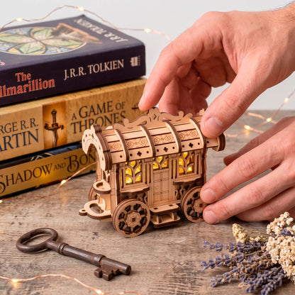 A person adjusting a glowing laser-cut plywood fairy cart illuminated from within right next to fantasy fiction book stacks.