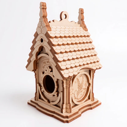 A close-up view of an unpainted wooden laser-cut plywood birdhouse highlighting the textured roof shingles and round entry.