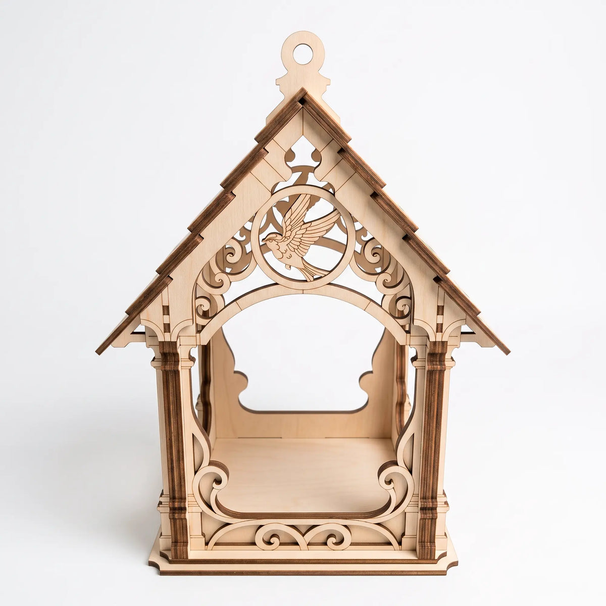 Front view of unpainted laser cut plywood bird feeder house with flying bird medallion and scrollwork on white backdrop