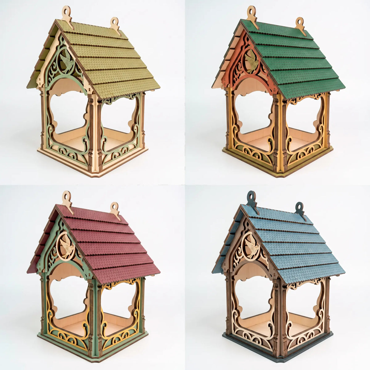 Four painted color variations of ornate laser cut plywood bird feeder house with shingled roofs against plain white.