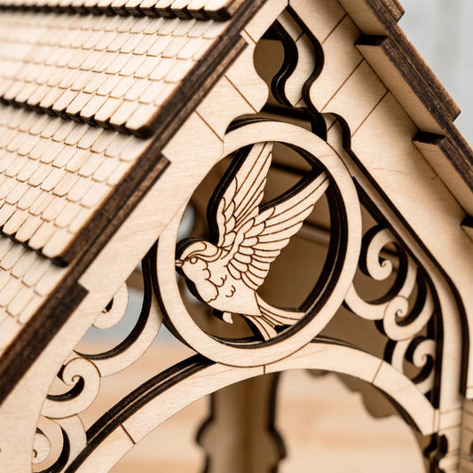 Macro close-up of intricate engraved flying bird emblem and layered gables on laser cut plywood bird feeder house.