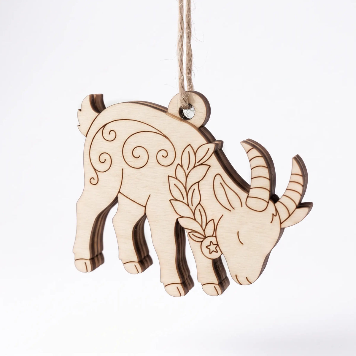 Laser cut plywood grazing goat ornament hanging on twine string with engraved leafy collar on plain white background.