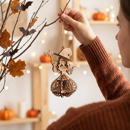 Woman hanging laser cut plywood witch ornament onto decorative autumn branch with paper bats and bokeh fairy lights.