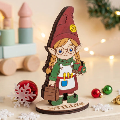 Painted laser cut plywood elf Tilly figurine holding a toy train, standing on a personalized wooden base.