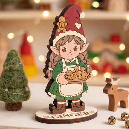 Painted laser cut plywood baker elf Ginger holding cookies next to felt tree and wooden deer on tabletop.