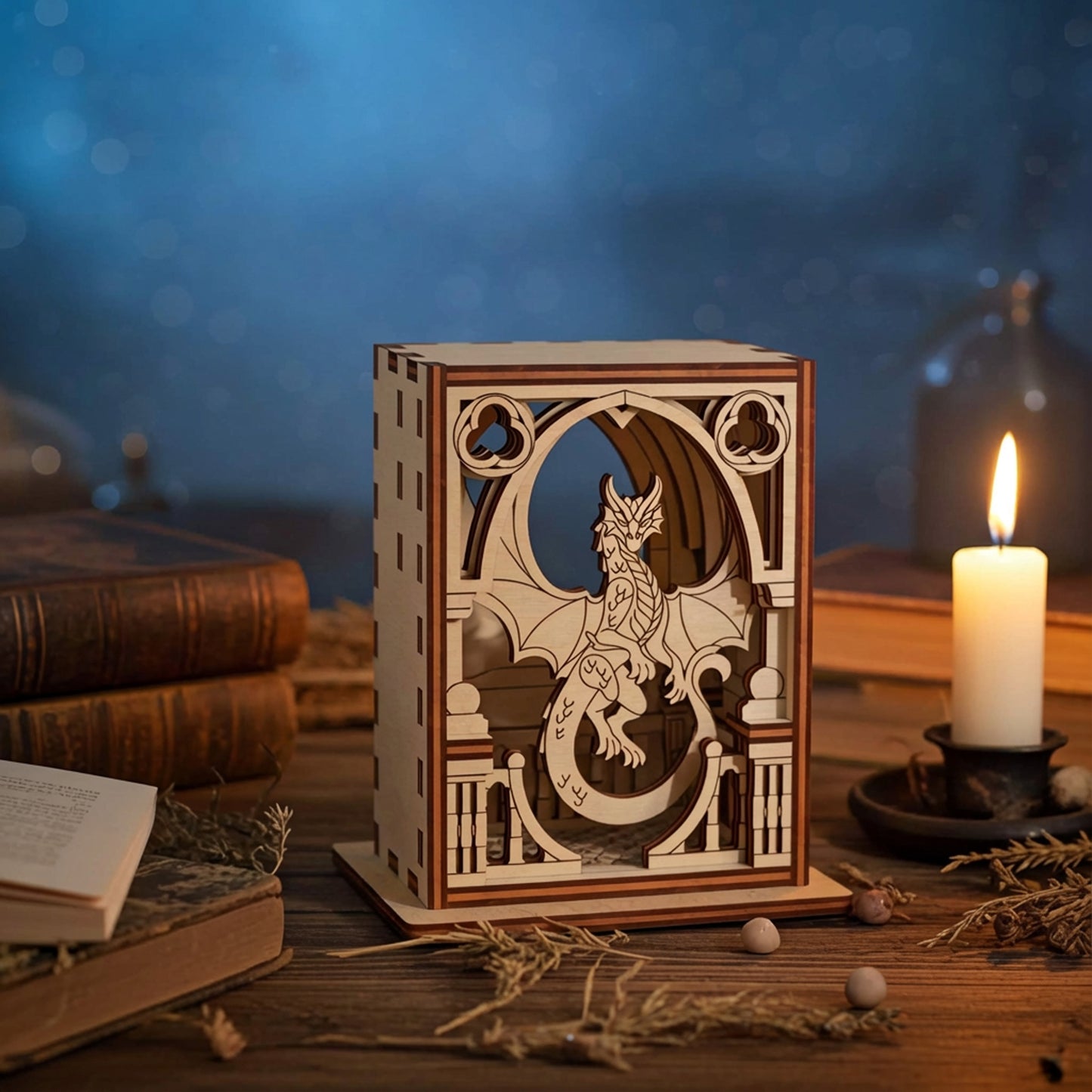 Wooden lantern with dragon laser cut design on a table with books and a candle.