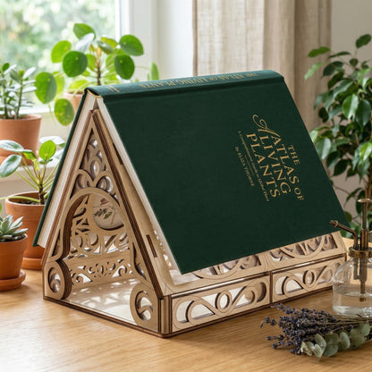 Decorative laser cut book stand with a green book titled 'Atlas of Plants' on a wooden surface with plants in the background.