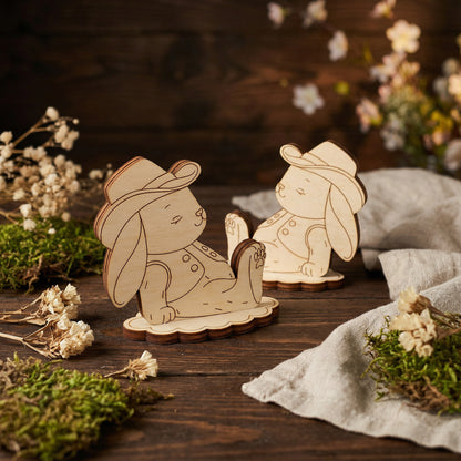 Wooden laser cut rabbit figurines with hats on a wooden surface with flowers and moss.