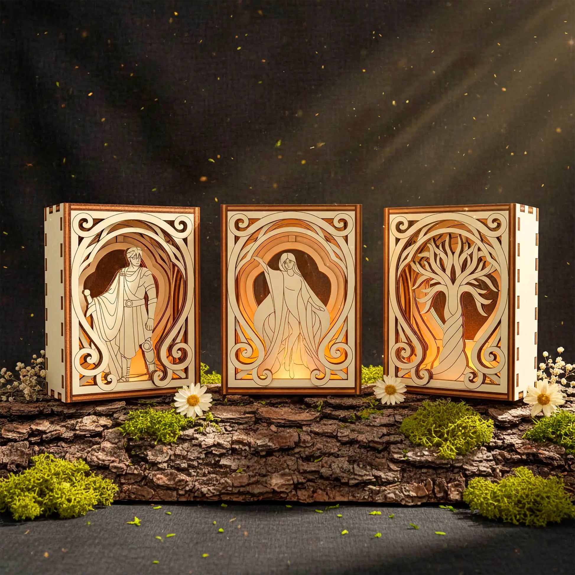 Three wooden laser cut book nooks with engraved designs of a warrior, a woman, and a tree, illuminated against a dark background.