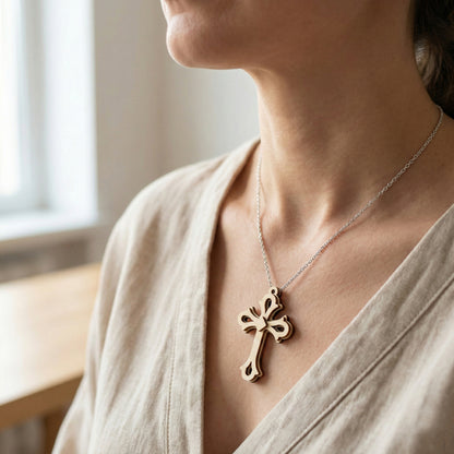 Person wearing a necklace with a laser cut cross pendant in a softly lit room.