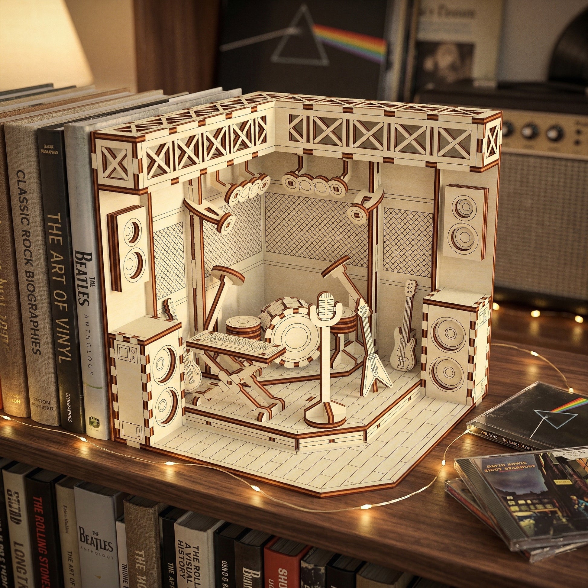 Wooden laser cut book nook model of a stage with musical instruments on a shelf with books and records.