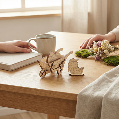 Wooden laser cut wheelbarrow and rabbit figure on a wooden table with a cup and book in the background.