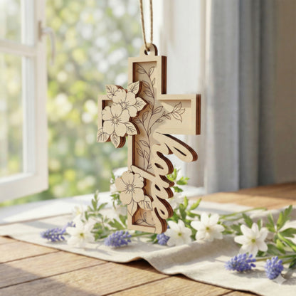 Laser cut cross with floral designs hanging on a table with flowers and a window in the background