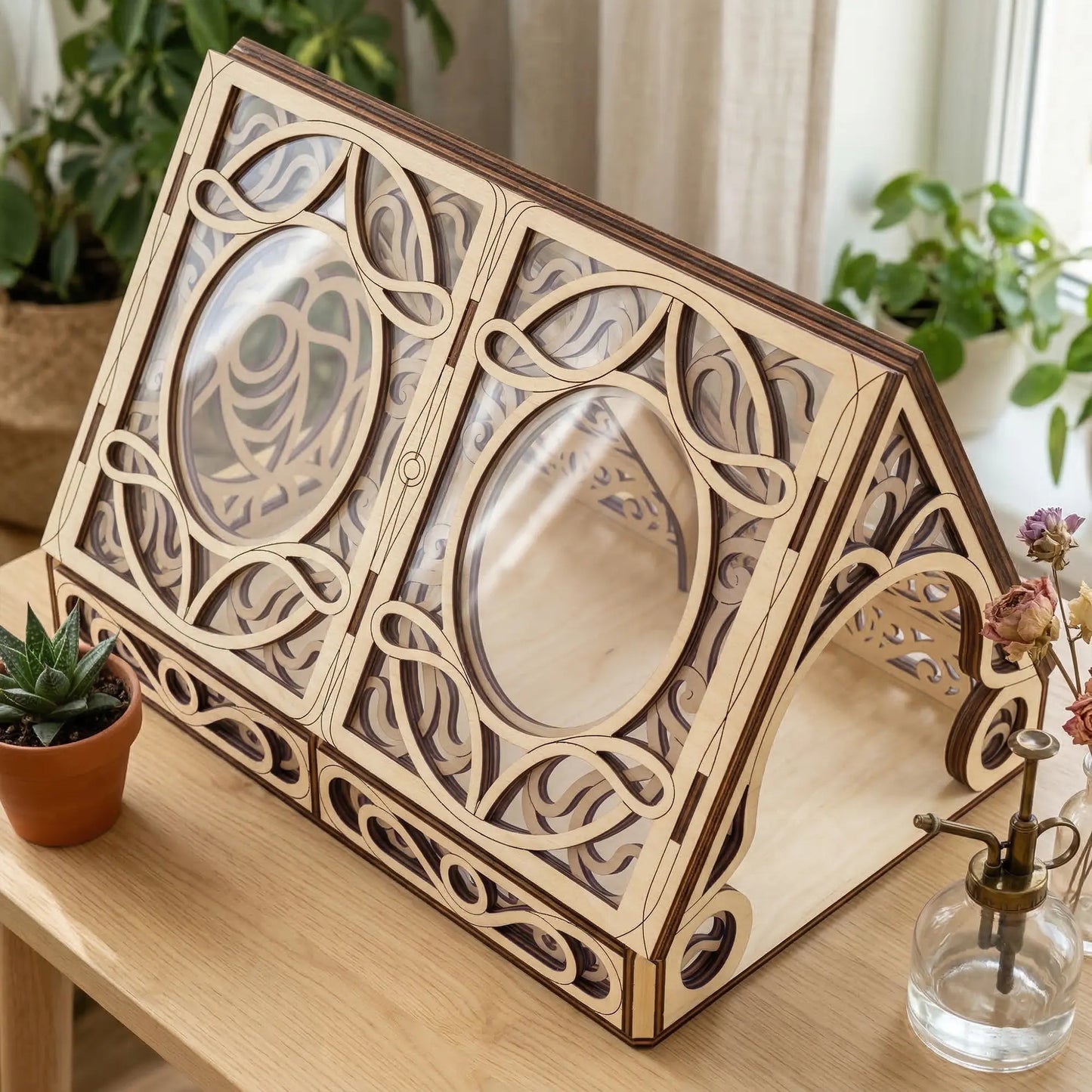 Wooden laser cut greenhouse with intricate designs on a wooden surface with plants in the background