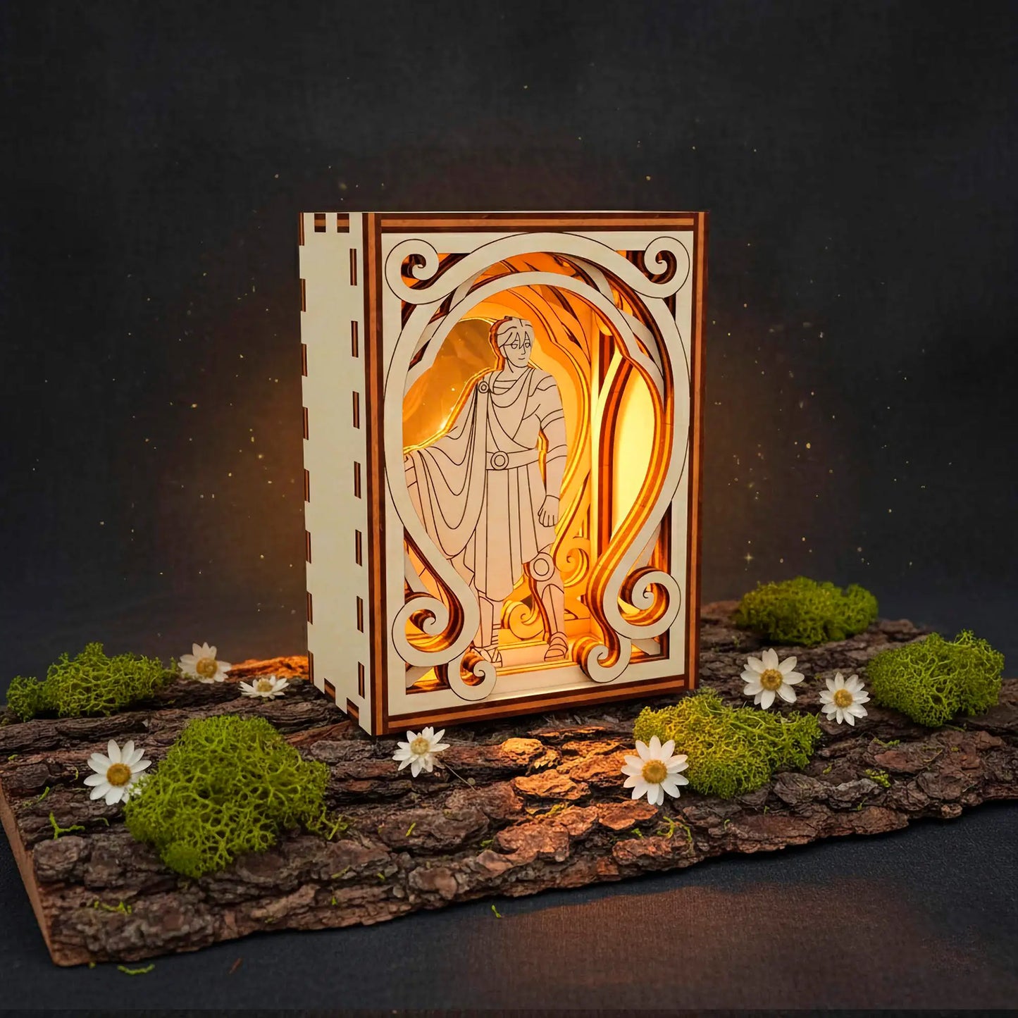 Decorative wooden laser cut box with a glowing interior featuring a classical design, surrounded by moss and flowers on a dark background.